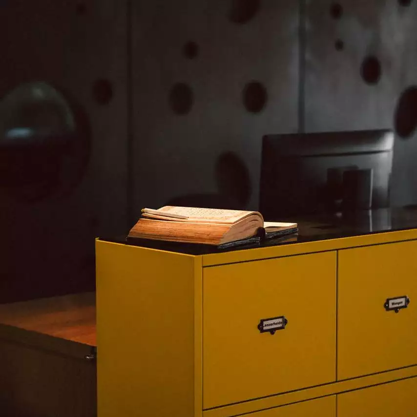Gästebuch an der Hotelrezeption im Après Post Hotel auf einem markanten gelben Counter mit beschrifteten Schubladen.